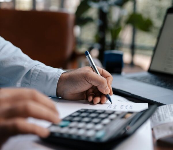 Free A person calculating finances with a calculator and pen on a desk indoors. Stock Photo